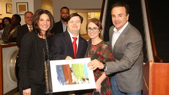 An artist holding TKC's 2020 'A Unique Perspective' Calendar at the Calendar Reception with a group of advocates.